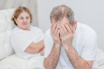 an elderly man cries, covering his face with his hands, against the background of a sitting wife