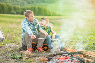 Naklejka na ściany i meble father and son talking at the fire and frying marshmallows. Space for text