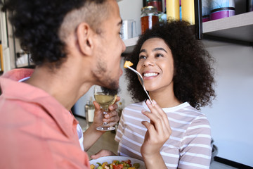 Young African-American couple tasting food in kitchen
