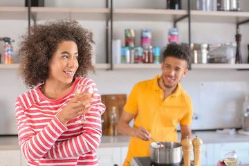 Young African-American woman drinking wine and her boyfriend cooking in kitchen