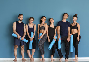 Fototapeta na wymiar Group of people with yoga mats near color wall