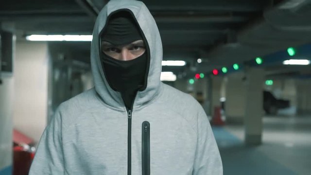 Portrait man in a black balaclava walks and looks menacingly at the camera.Slow mo