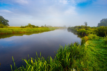 Colorful sunrise near foggy river in rural area