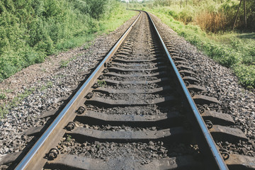 Fototapeta premium Rail tracks in the green field. Railway transport industry. Empty road on summer day. Travel lifestyle motivation photo.