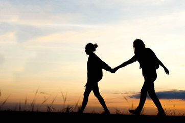 Silhouette of woman walking holding hand during a beautiful sunset.