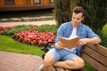 Young man reading book while sitting on wooden bench in park