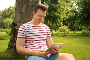 Obraz premium Young man with tablet PC sitting near tree in park