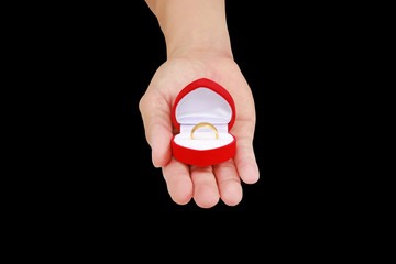 Hand holding red gift box with gold wedding ring isolated on black background.