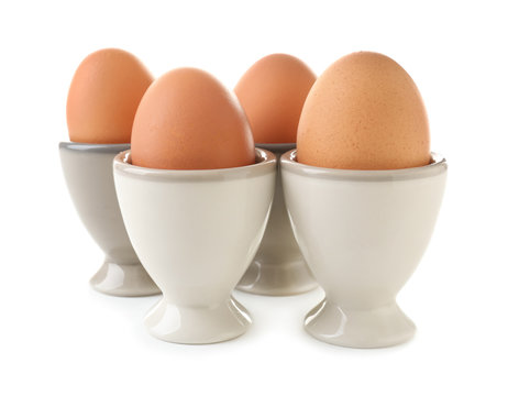 Ceramic holders with chicken eggs on white background
