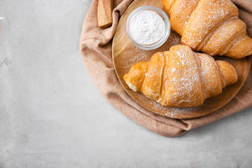 Wooden board with tasty croissants and sugar powder on table