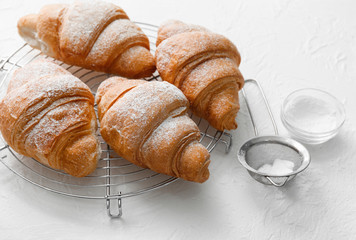 Cooling rack with fresh tasty croissants on light textured background