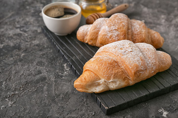 Board with tasty croissants on grey textured background