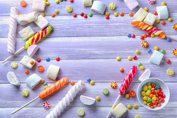 Frame made of delicious lollipops with marshmallows on color wooden background