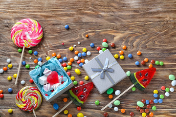 Composition with colorful candies and gift box on wooden background