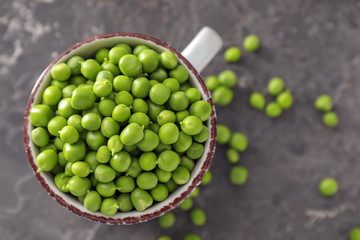 Cup with delicious fresh green peas on grey textured background