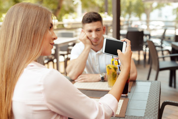 Young couple drinking coffee in a cafe. Serious man worriedly looking while his girl using smart phone