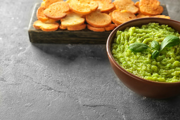 Bowl with tasty guacamole and bread chips on grey textured background