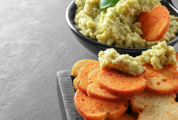 Bowl with tasty guacamole and bread chips on grey textured background