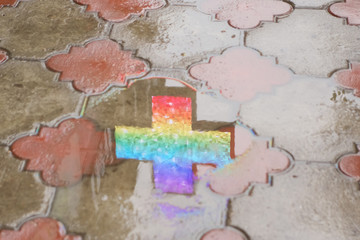 Reflection in a puddle of an advertising light shield in the form of a cross on a sidewalk tile