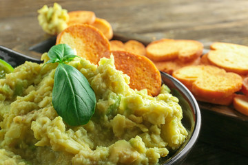 Bowl with tasty guacamole and bread chips on table