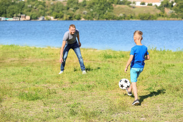 Happy father and son playing football near river