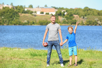 Naklejka na ściany i meble Happy father and son with rugby ball near river