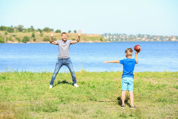Obraz premium Happy father and son playing rugby near river