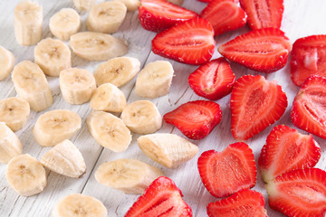 Ripe sliced strawberries and bananas on light wooden background