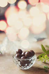 Chocolate dragee in a glass bowl on peachy cloth. Sparkling lights in the background and copy space