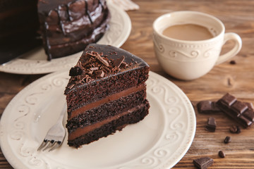 Plate with piece of delicious chocolate cake and cup of coffee on wooden table