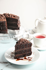 Plate with piece of delicious chocolate cake and cup of tea on light table