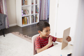 Naklejka premium Young Boy Sitting At Desk In Bedroom Using Digital Tablet To Make Video Call