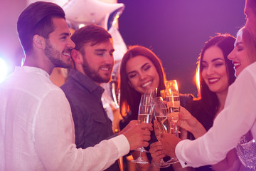 Young people clinking glasses with champagne at birthday party in club