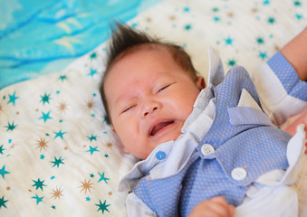 Crying infant baby boy in suit lying on bed.
