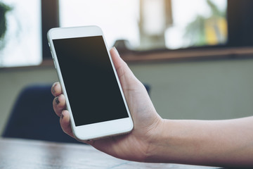 Mockup image of a woman holding white mobile phone with blank black screen on wooden table