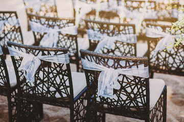 The back side of black wooden chairs with white organza sash decoration for beach wedding venue