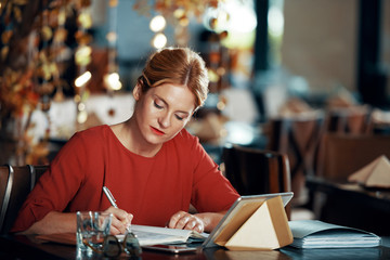 Fototapeta premium Serious female writer working at the cafe while waiting for her order. She is writing ideas in her notebook