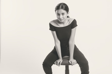 Obraz premium Portrait of cool happy brunette fashionable teenage girl, casual hairdo and pink makeup. Woman smile in studio isolated on white background sitting on chair monochrome