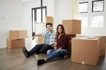 Fototapeta na wymiar Portrait Of Happy Couple Sitting On Floor Surrounded By Boxes In New Home On Moving Day