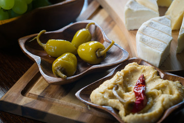 A set of appetizers of various types of cheese and marinated peppers and hummus paste