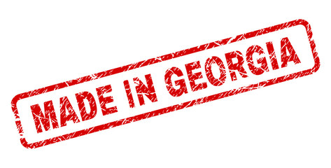 MADE IN GEORGIA stamp seal watermark with scratced style. Red vector rubber print of MADE IN GEORGIA text with retro texture. Text label is placed inside rounded rectangle frame.
