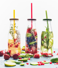 Infused water in bottles with drink straw and ingredients on white background, front view. Water...