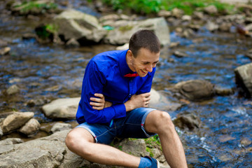 Portrait of young smiling handsome man in blue shirt near forest river. Emotions concept