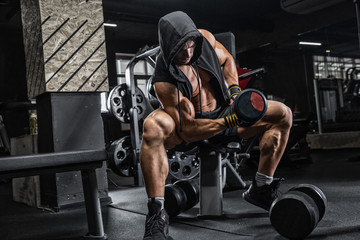 The brutal man is training the biceps on the bench, using a dumbbell. Concept - personal trainer, diet, sports nutrition, crossfit, styrodes, dumbbells, bodybuilding, weightlifting, gym.