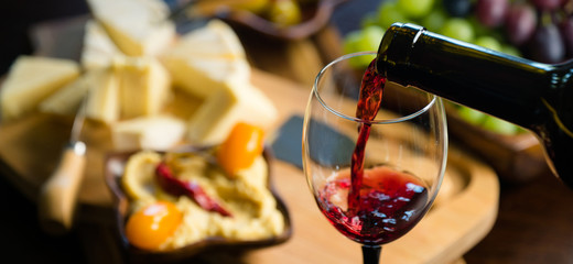 Pouring red wine into the glass in the background composition of appetizers