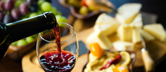 Pouring red wine into the glass in the background composition of appetizers
