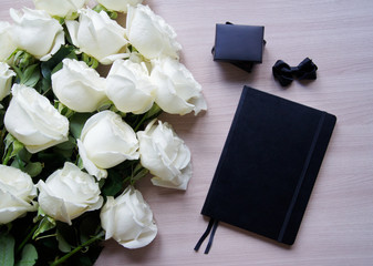 Stylish feminine photo with a bouquet of beautiful white roses, black notebook and small jewelry box. Blogging lifestyle photo.