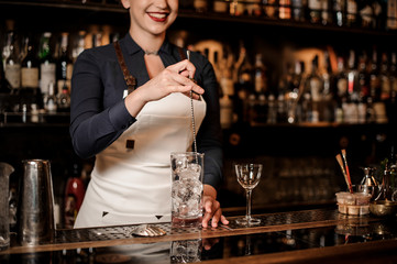 Professional female bartender mixing an ice in the glass