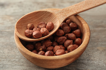 Bowl and spoon with fresh tasty hazelnuts on wooden table