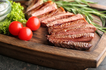 Tasty cut steak, rosemary and tomatoes on wooden board, closeup